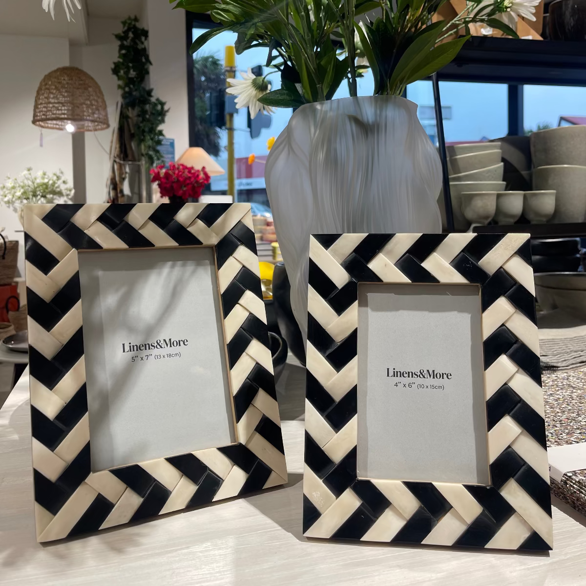 Two black and white chevron patterned picture frames with a vase of flowers in the background.