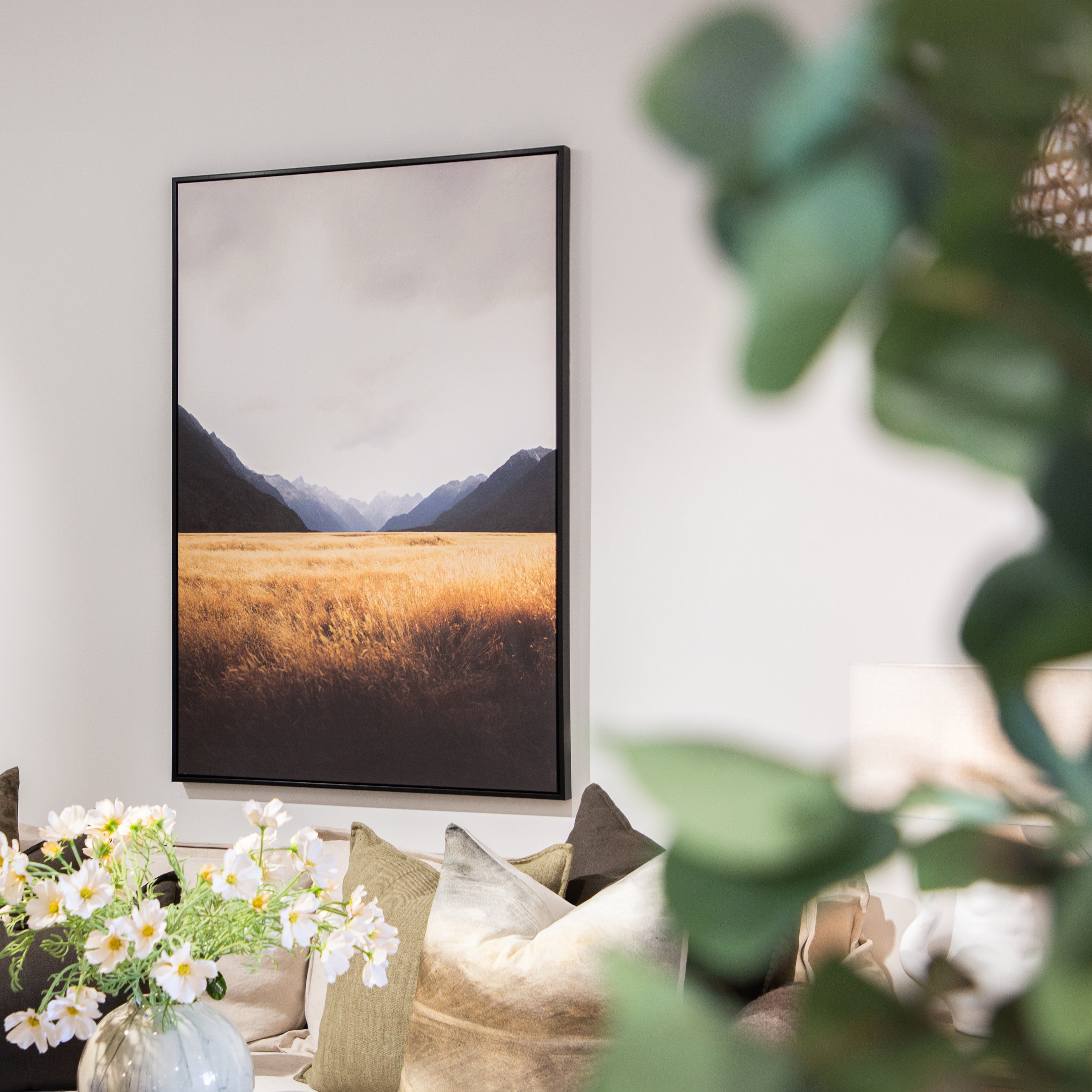 Living room with a framed landscape print on the wall, flowers on a table, and a couch.
